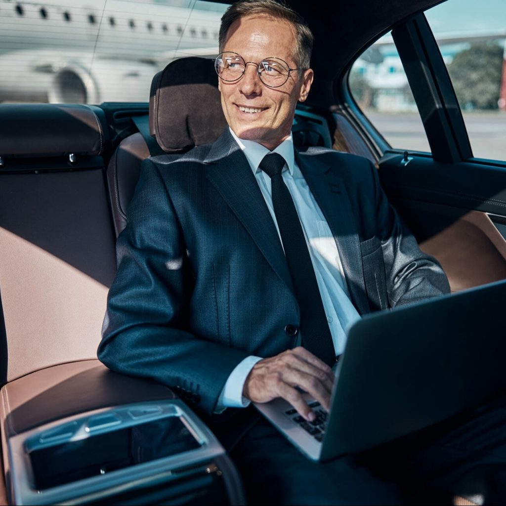 cheerful businessman with laptop in car at airport 2021 09 03 21 02 41 utc e1670821770815